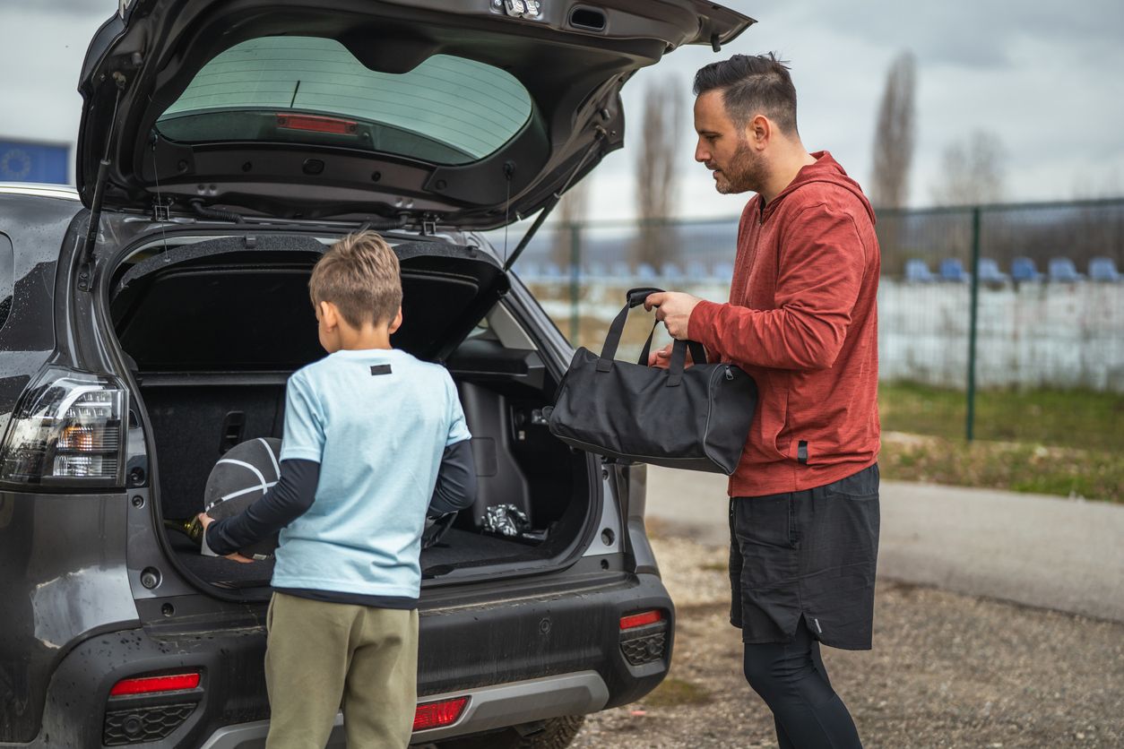 Parent and child packing sports equipment into a vehicle before traveling to a youth sports tournament.