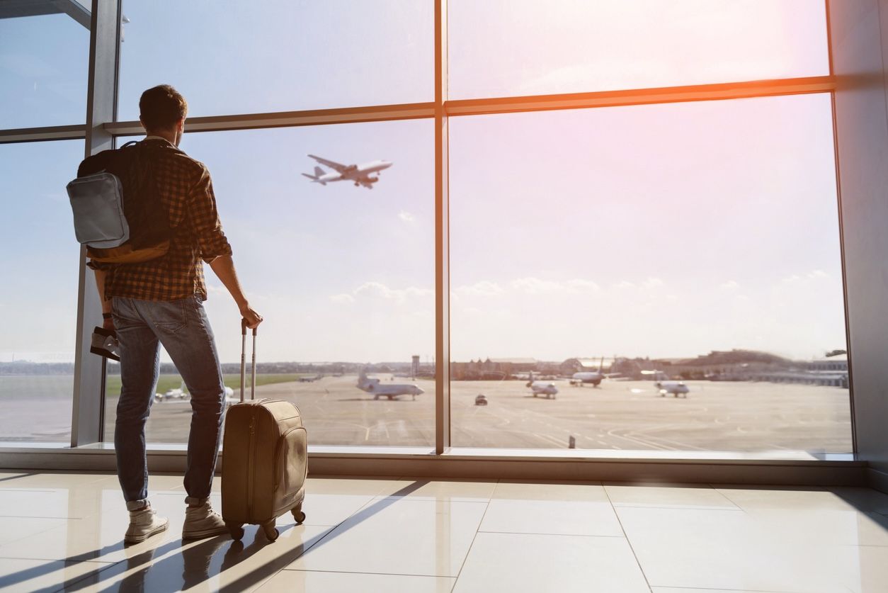 Traveler at airport watching a plane take off through terminal window during layover.