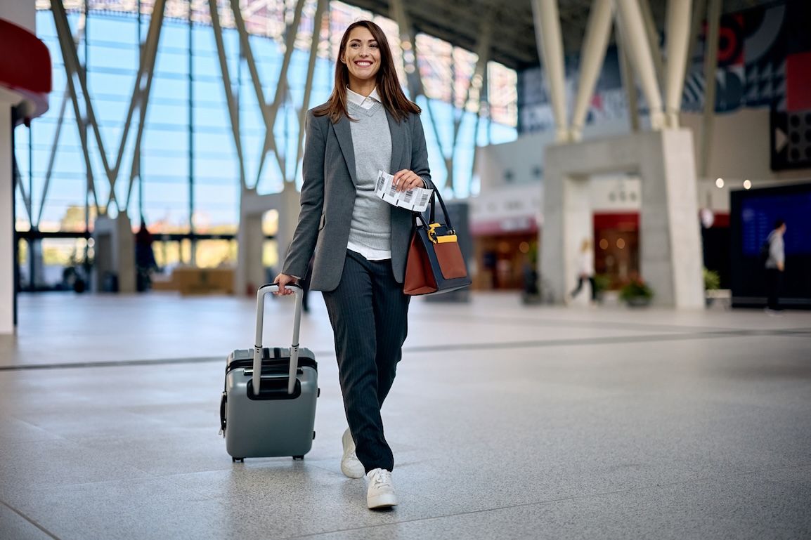 Smiling traveler walking through a modern airport terminal with a rolling suitcase, representing easy airport access and stress-free hotel transportation in Nashville.