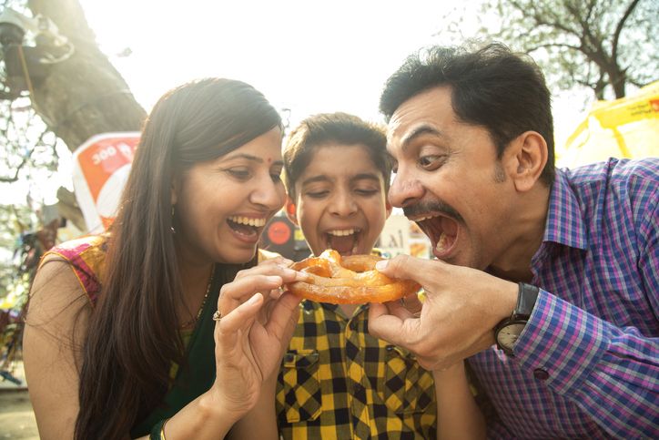 Family enjoying delicious food together at a local outdoor food fair, smiling and sharing a fun community moment.