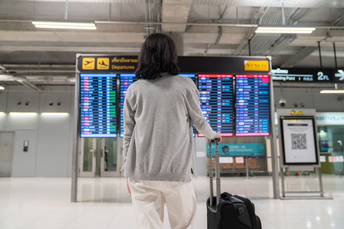 Woman checking flight information on a departure board during airport layover