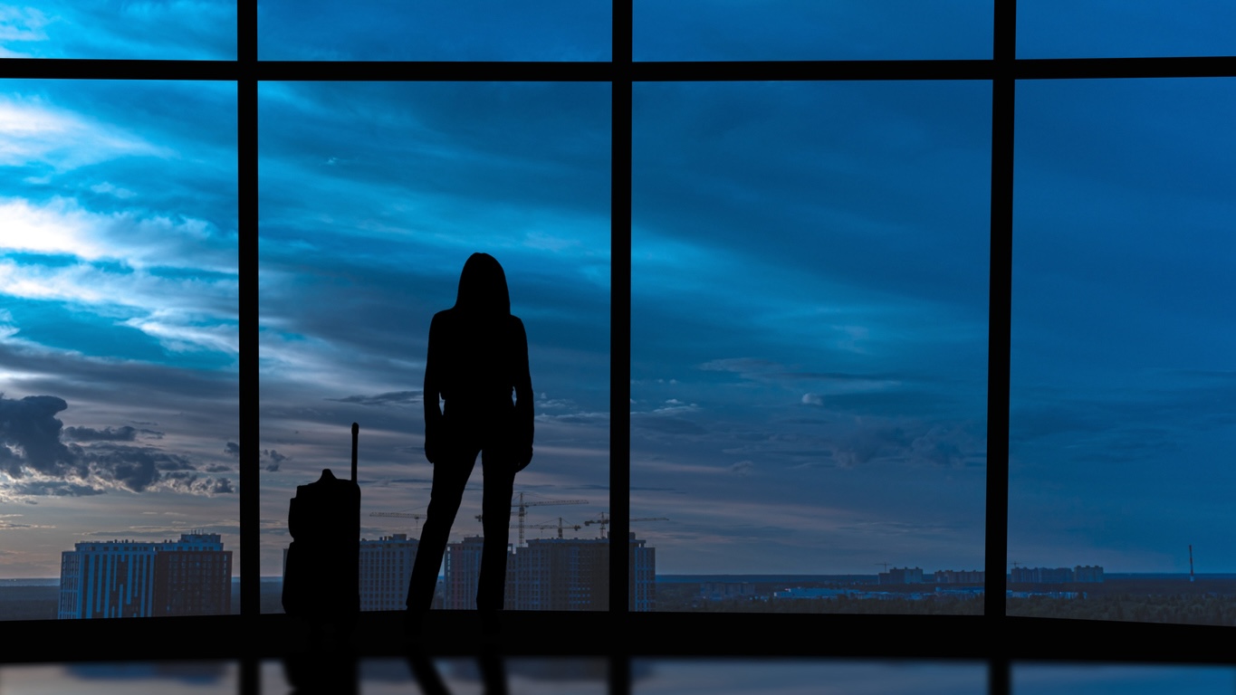 Silhouette of woman with suitcase looking out airport window at night, arriving for a late flight in Nashville